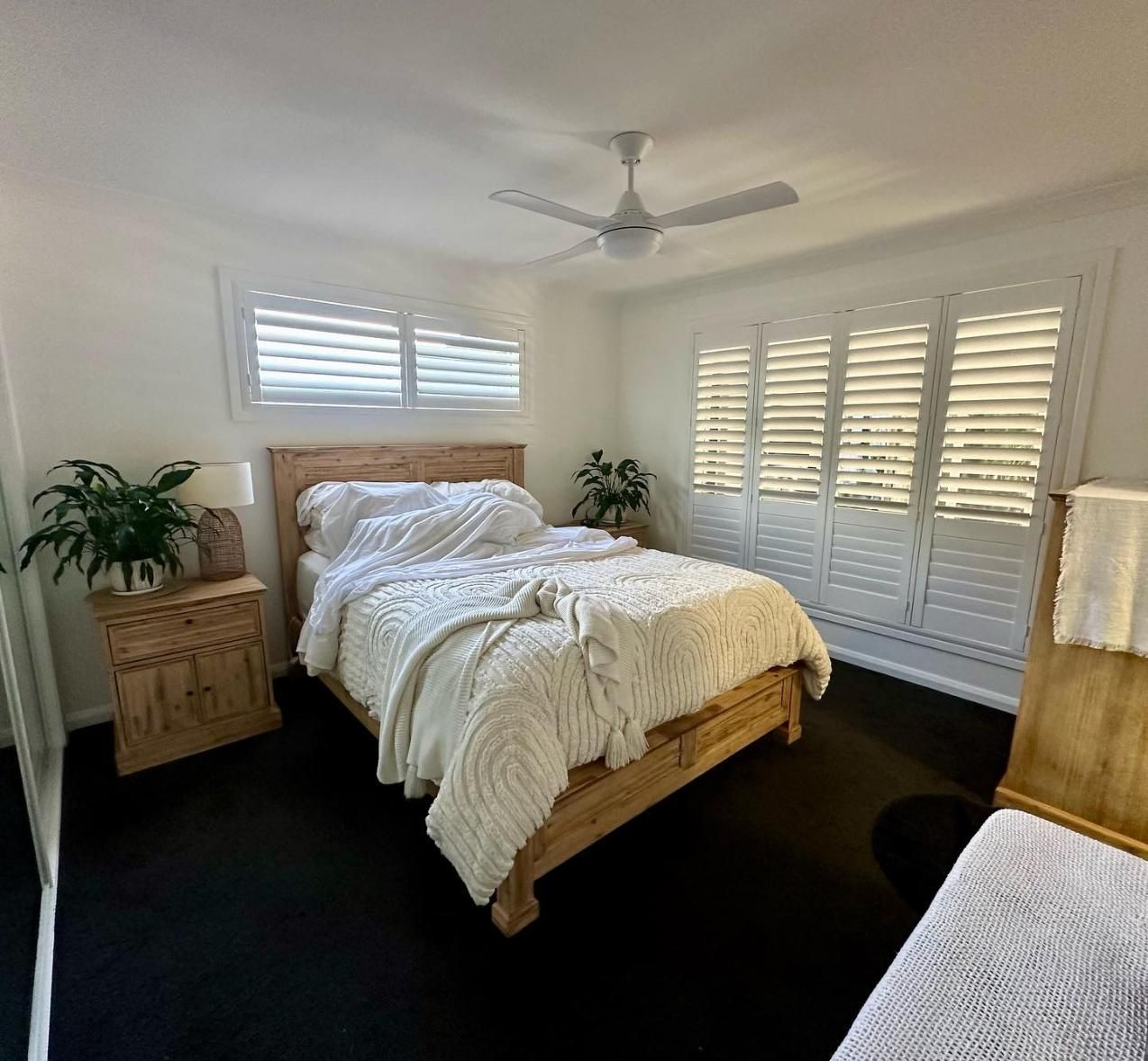 A Bedroom With a Bed, Nightstand, Ceiling Fan and Shutters — TT Shutters & Shading In Mullumbimby, NSW