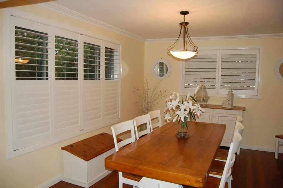 A Dining Room With a Wooden Table and White Chairs — TT Shutters & Shading In Murwillumbah, NSW