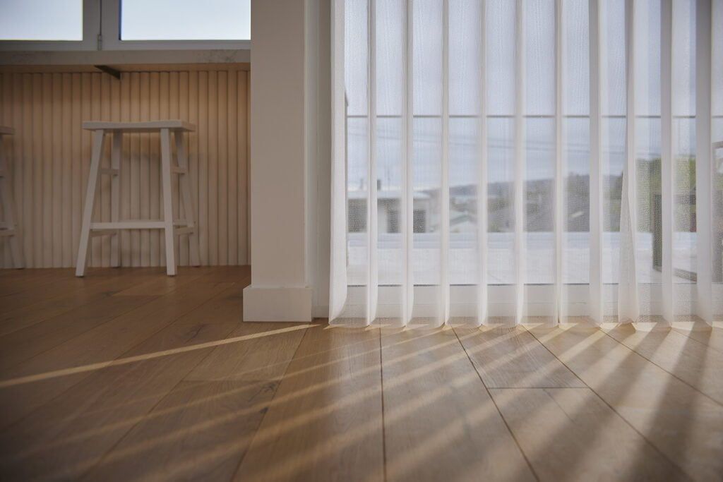A Room With a Wooden Floor and White Vertical Blinds on the Windows — TT Shutters & Shading In Ballina, NSW