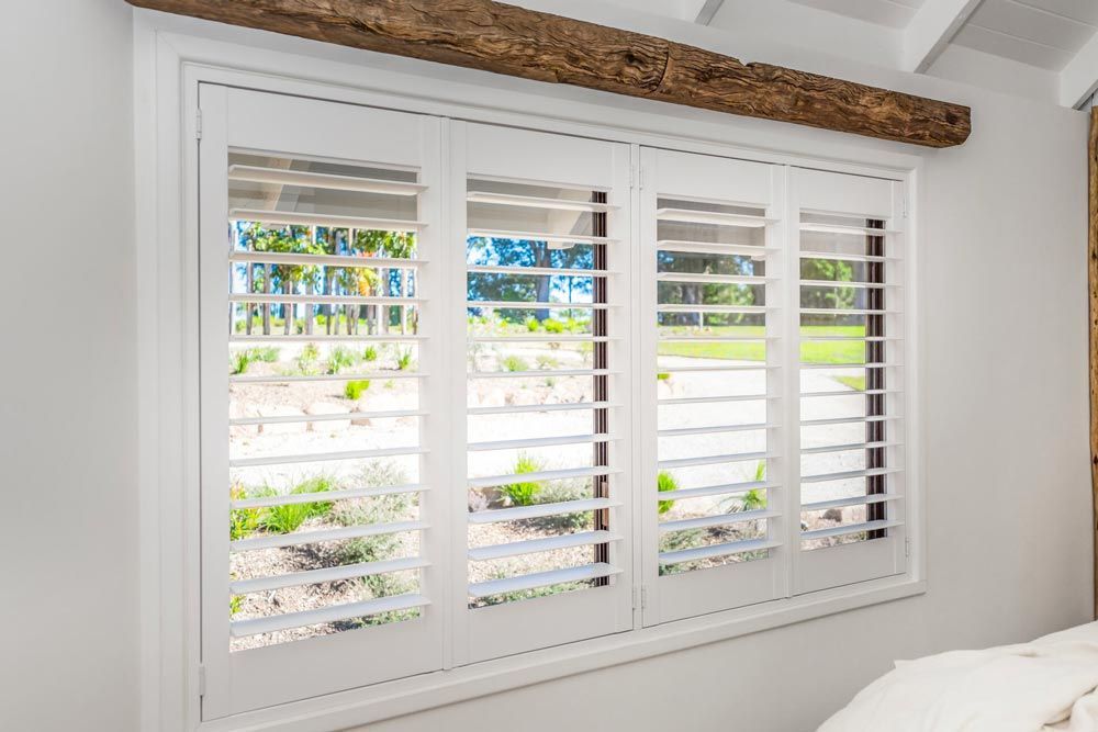 A Bedroom Window With White Shutters and a Wooden Beamed Ceiling — TT Shutters & Shading In Yamba, NSW