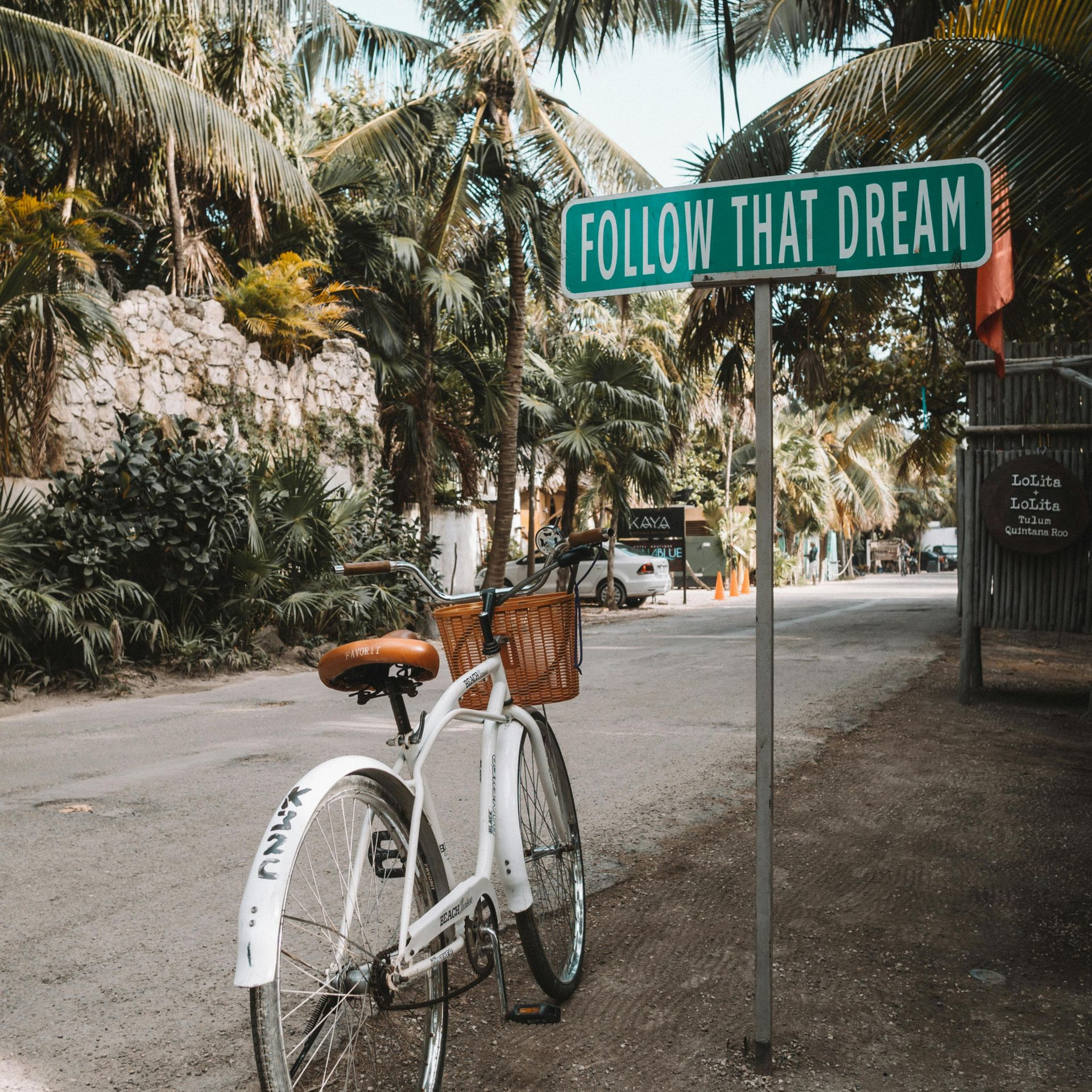 A white bicycle with a basket stands next to a green sign that reads 