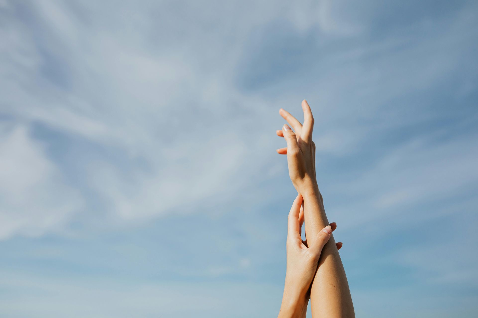 Two hands reaching upward against a clear blue, cloudy sky.