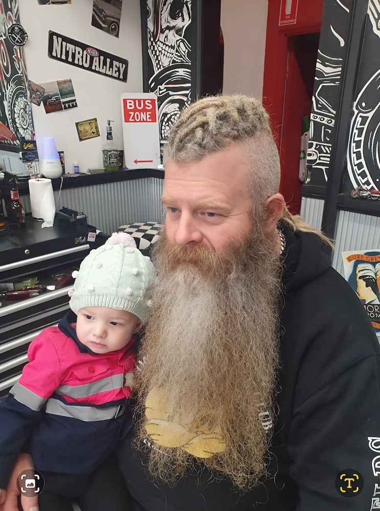A Man With A Beard Is Holding A Baby In His Arms — The Barber Social In Raymond Terrace, NSW