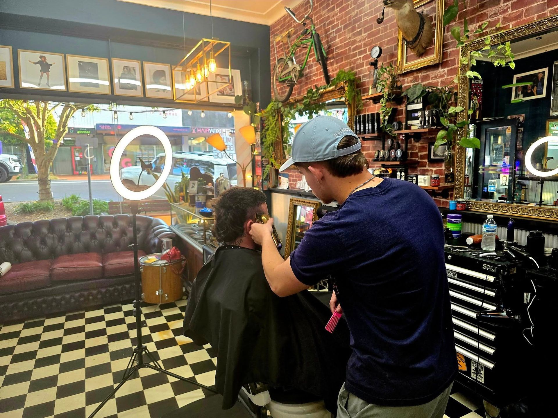A Barber Gives a Haircut in A Shop with A Red Brick Wall and Checkered Floor — The Barber Social In Raymond Terrace, NSW