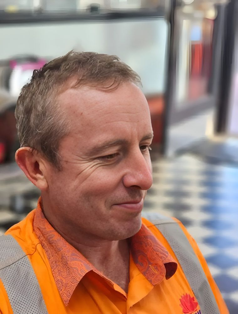 A Man Wearing An Orange Shirt And Safety Vest Is Smiling — The Barber Social In Raymond Terrace, NSW