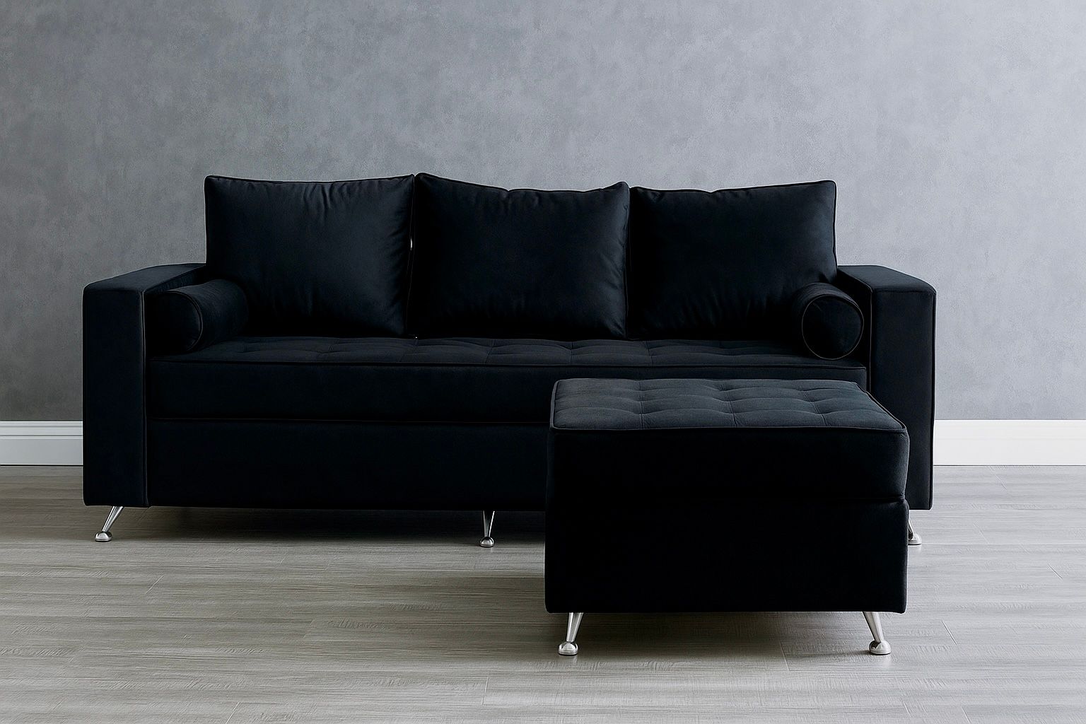 Un sofá de terciopelo negro con un puf a juego sobre patas plateadas, apoyado contra una pared gris.