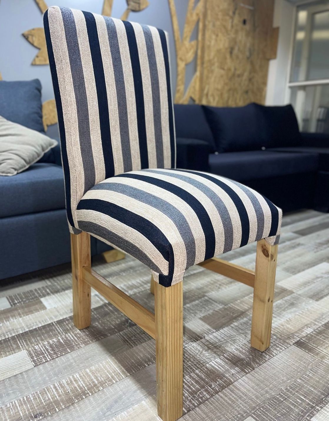 Una silla de comedor de madera con respaldo alto y asiento tapizado en tela de rayas verticales azul marino, gris y crema.