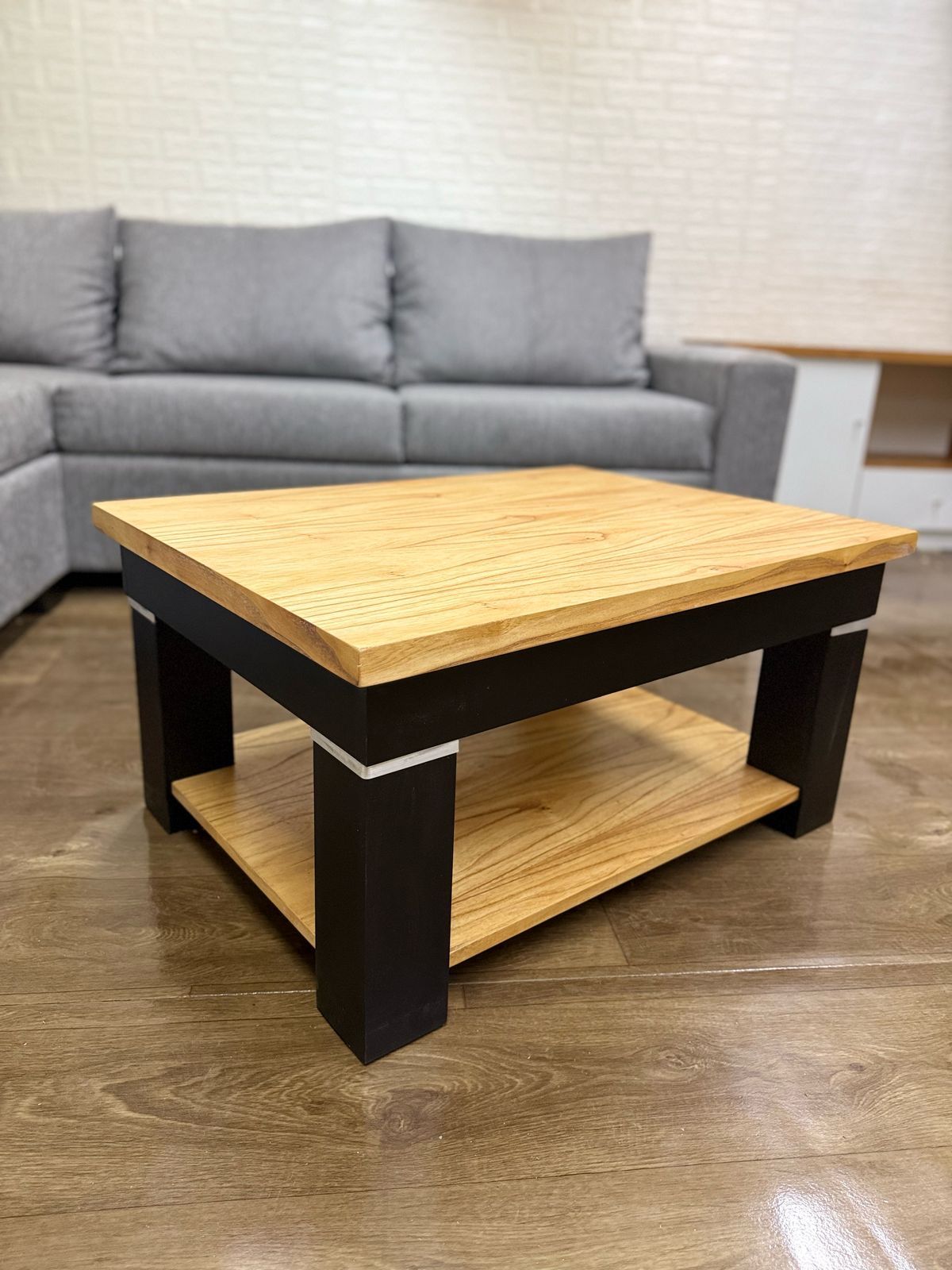Una mesa de centro de madera con base blanca y estante inferior, colocada delante de sofás grises y beige