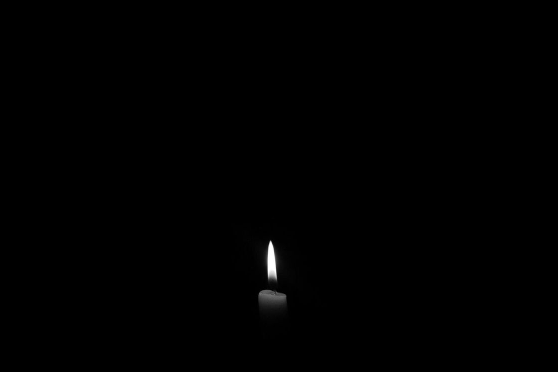 La llama de una sola vela encendida brilla en el centro de un fondo completamente negro.