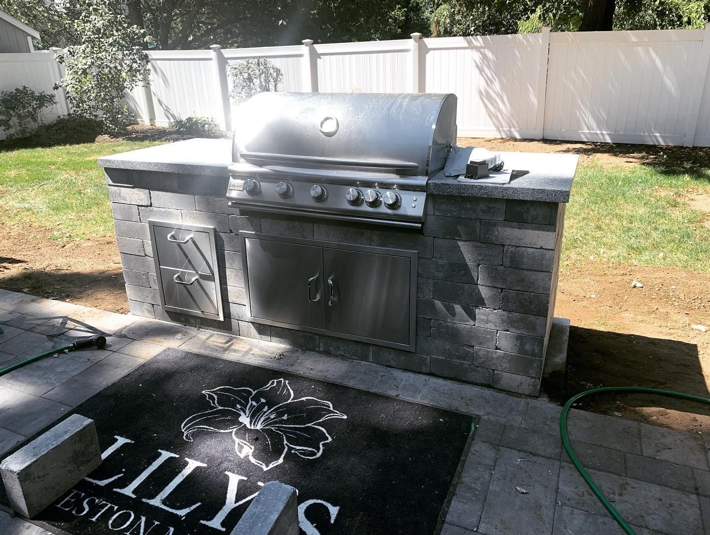 Outdoor grilling station made of stone with a stainless steel grill and storage compartments.