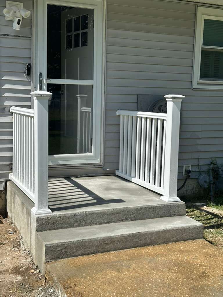 White porch with handrails and steps leading to a glass door on a gray house.