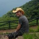 A man wearing a cowboy hat is sitting on a rock with a dog.