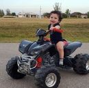 A little boy is riding a four wheeler on a road.