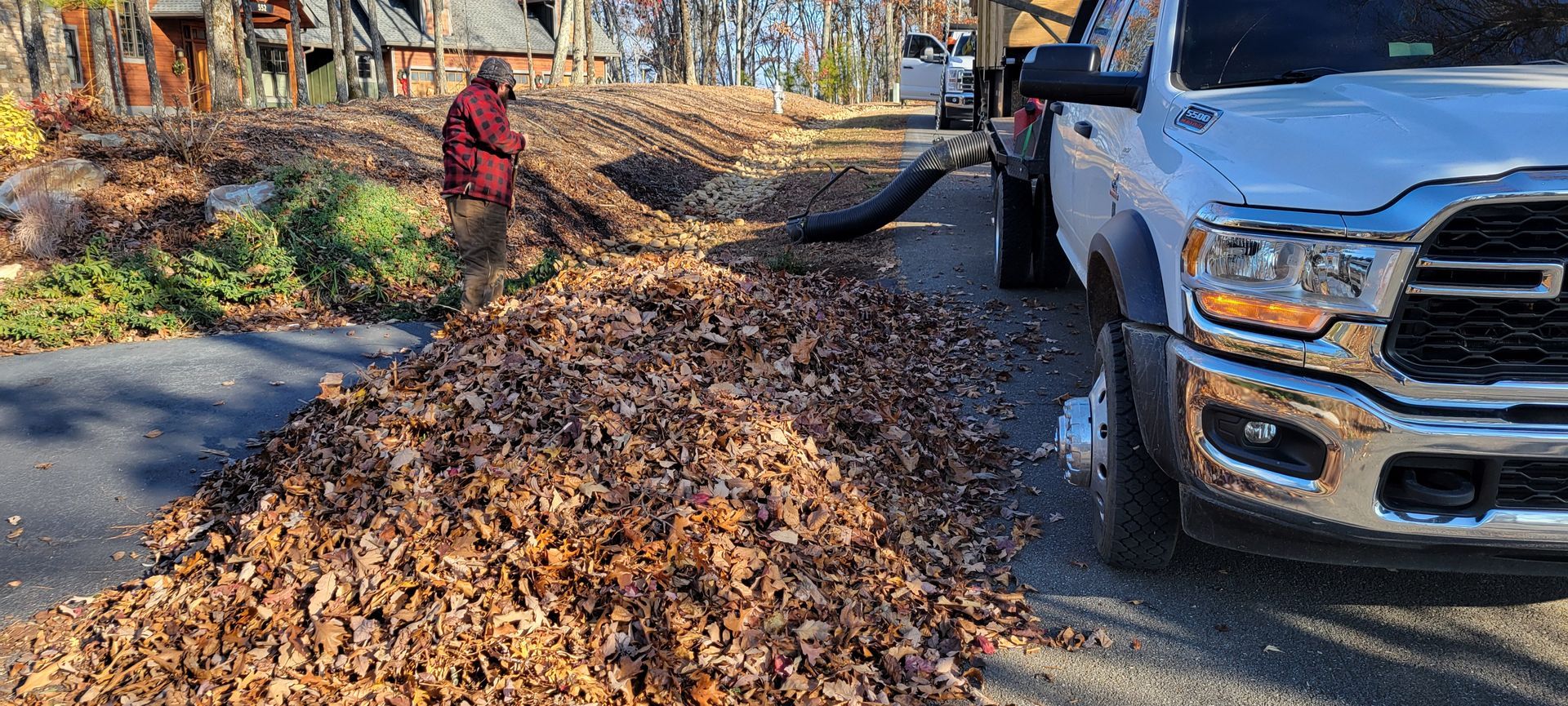 Man raking leaves into a tube connected to a white truck on a road.