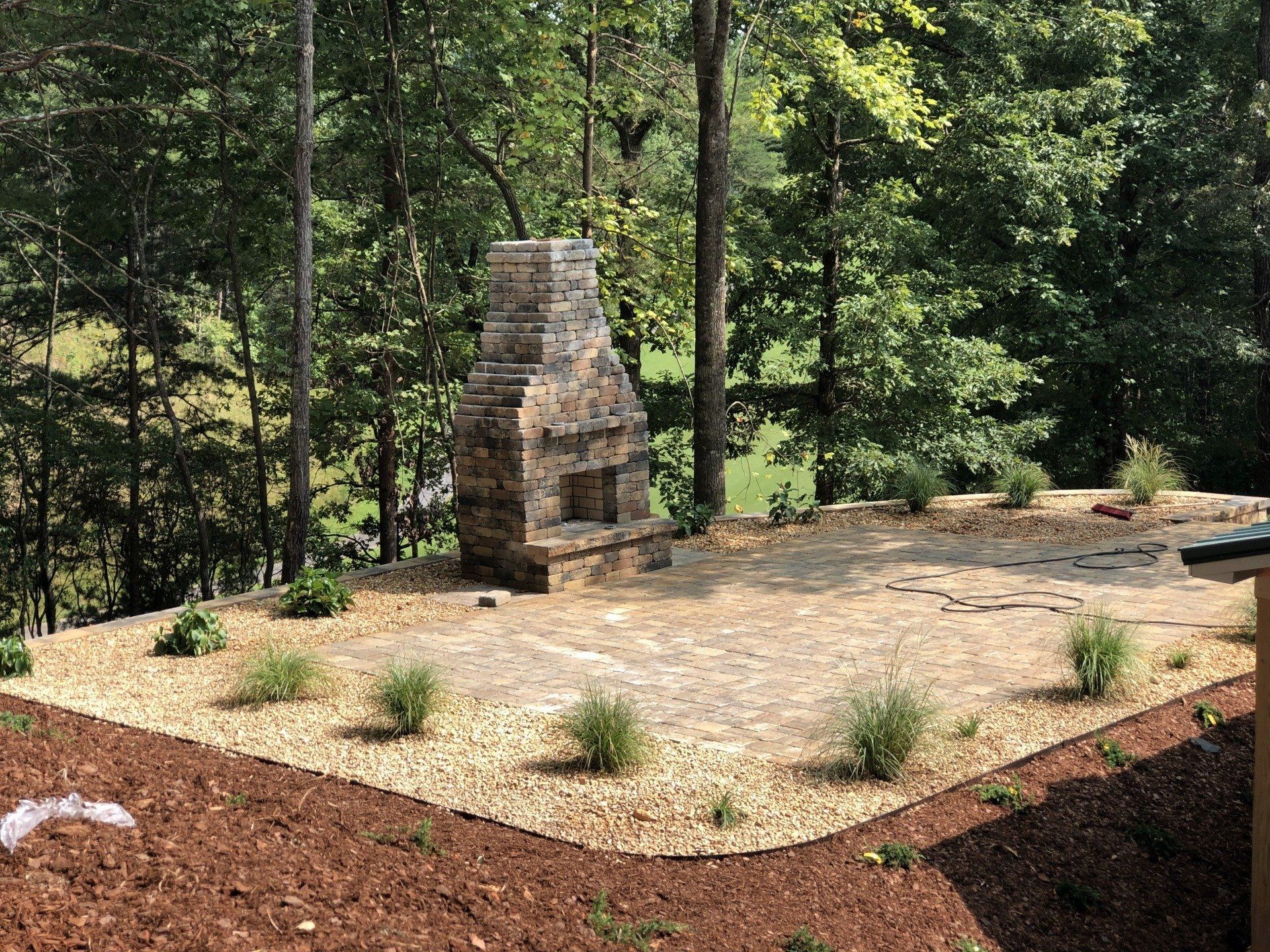 A stone fireplace sits in the middle of a lush green forest