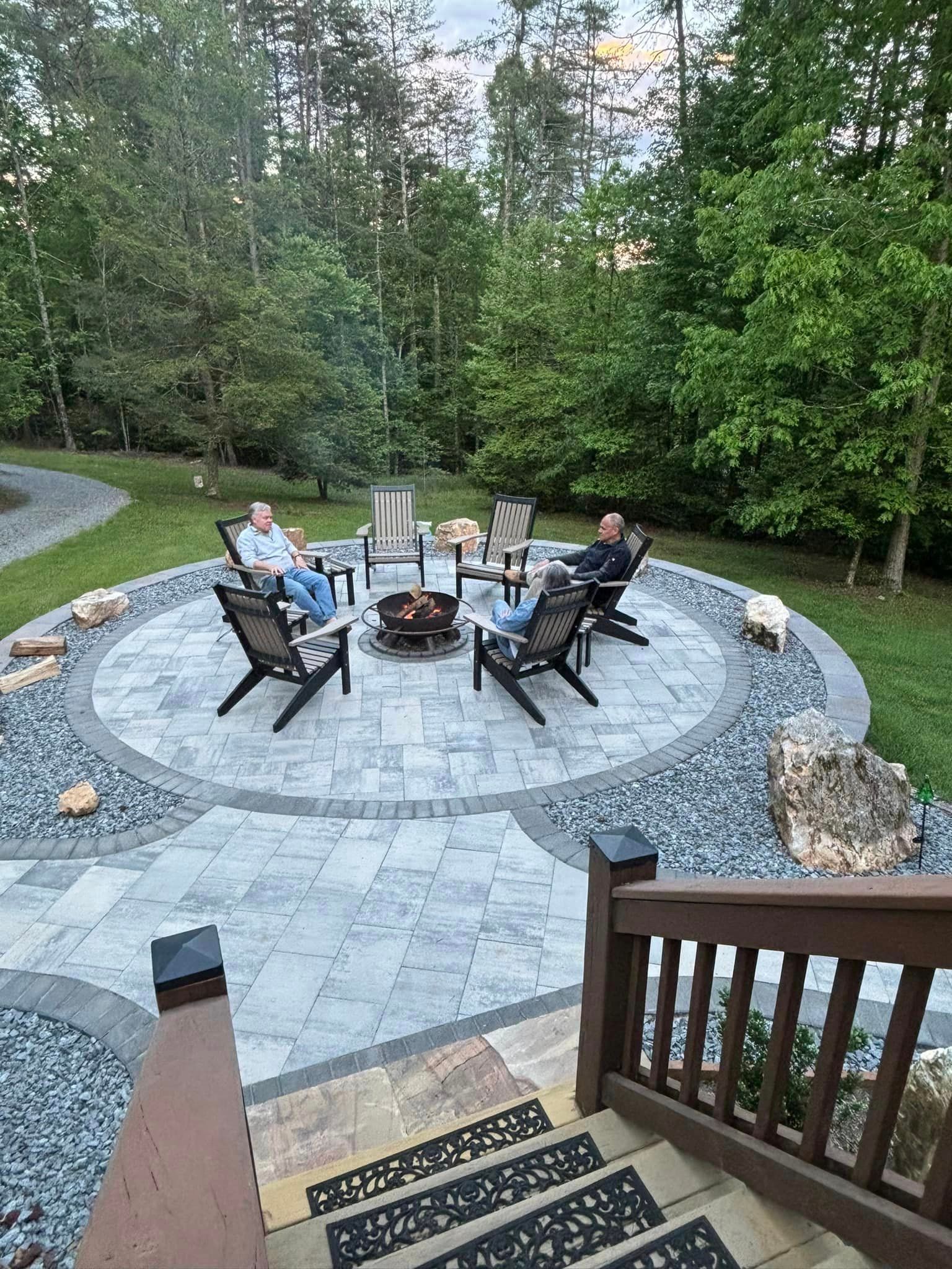 A group of people are sitting around a fire pit on a patio.