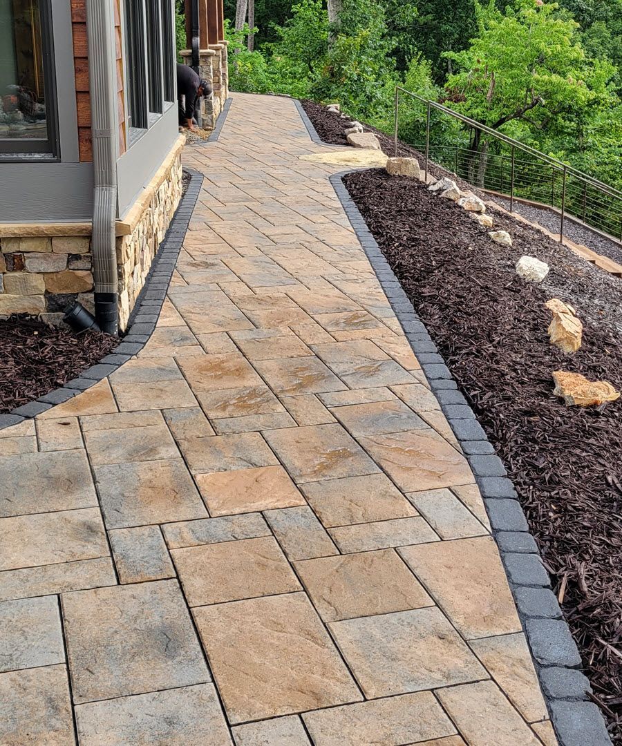 Stone paver walkway with dark border alongside a building and landscaping.