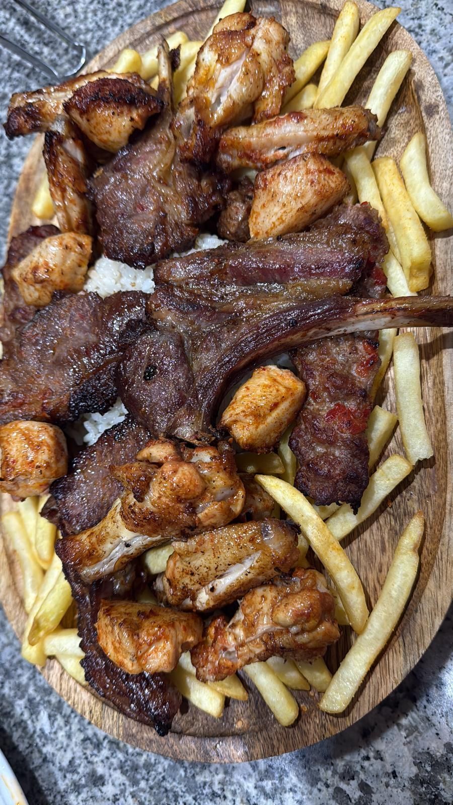 Carne alla griglia e ali di pollo con patatine fritte su un vassoio di legno.