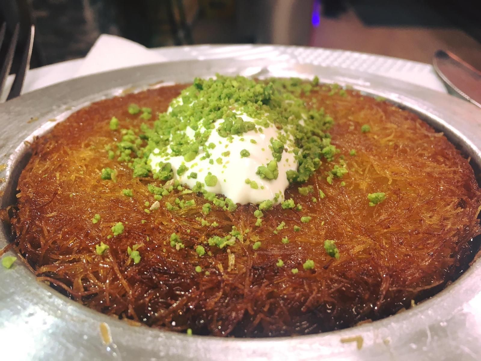 Dessert Kunefe guarnito con panna e pistacchi, servito su un piatto di metallo.