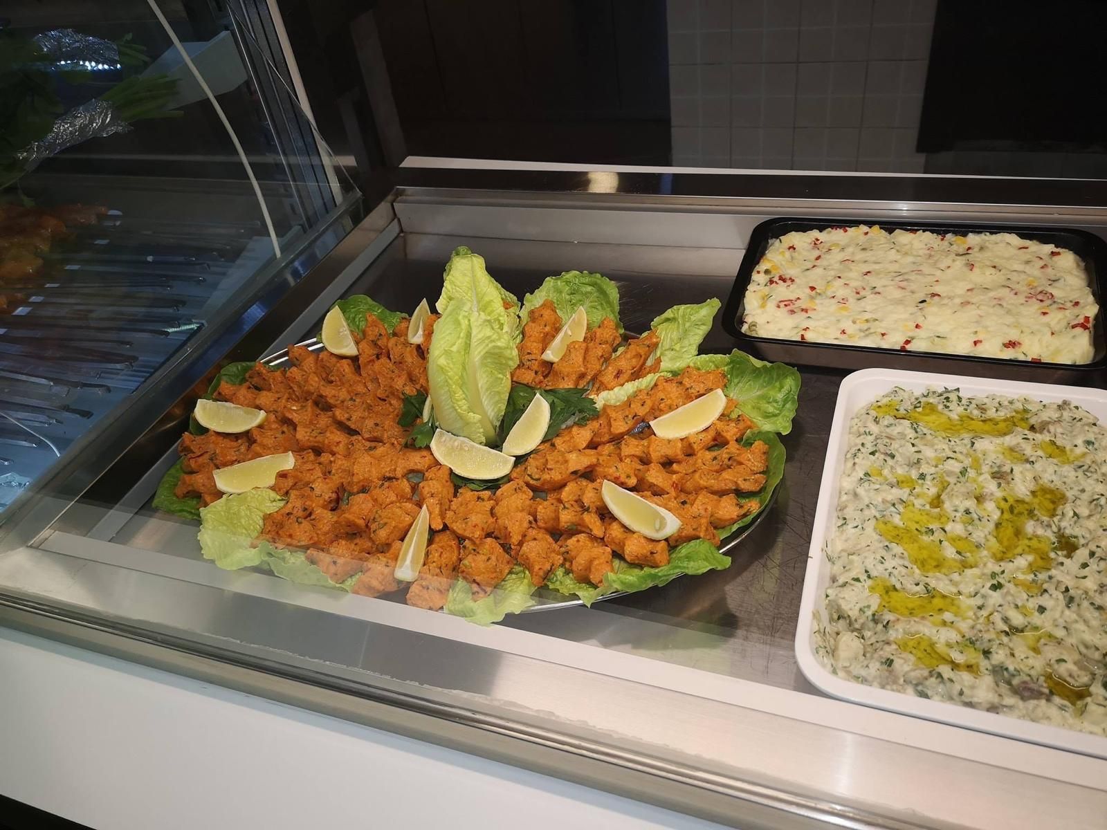 Vetrina con cibo: piatti rossi e verdi, uno con lattuga e limone, uno con insalata di patate bianche e uno con riso verde.