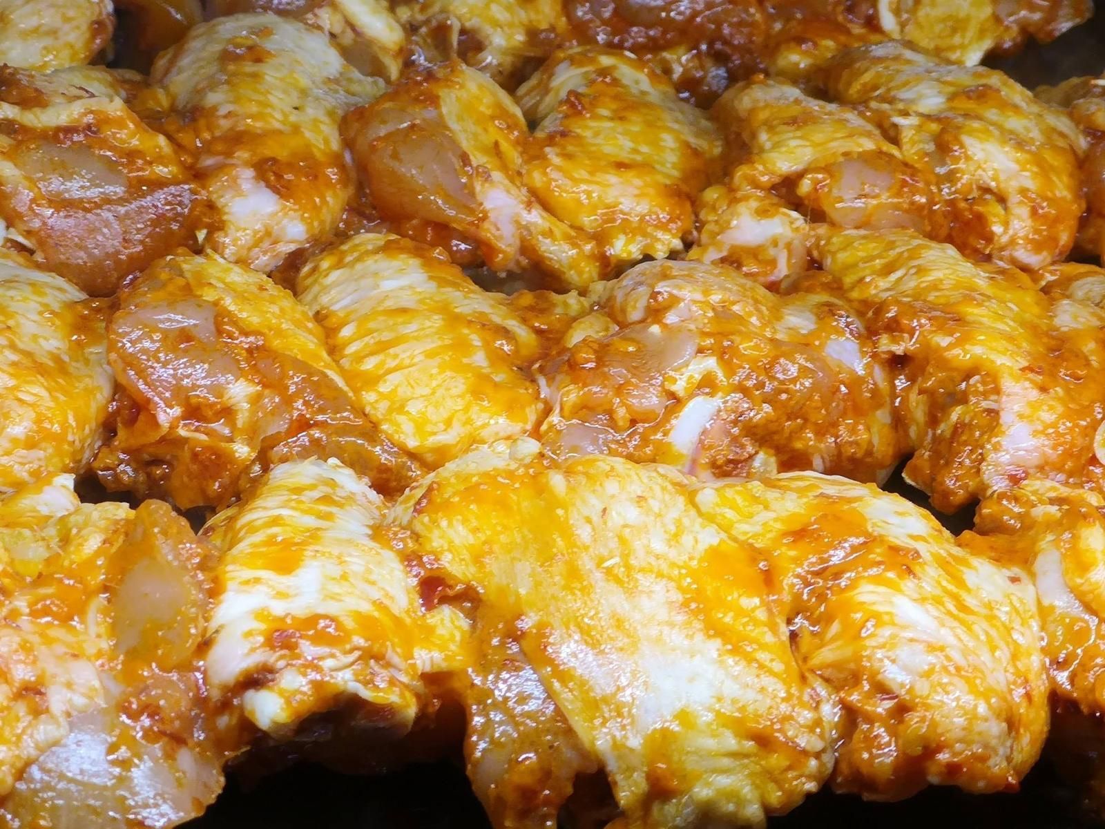Alette di pollo crude ricoperte da una vivace marinata arancione, pronte per la cottura.
