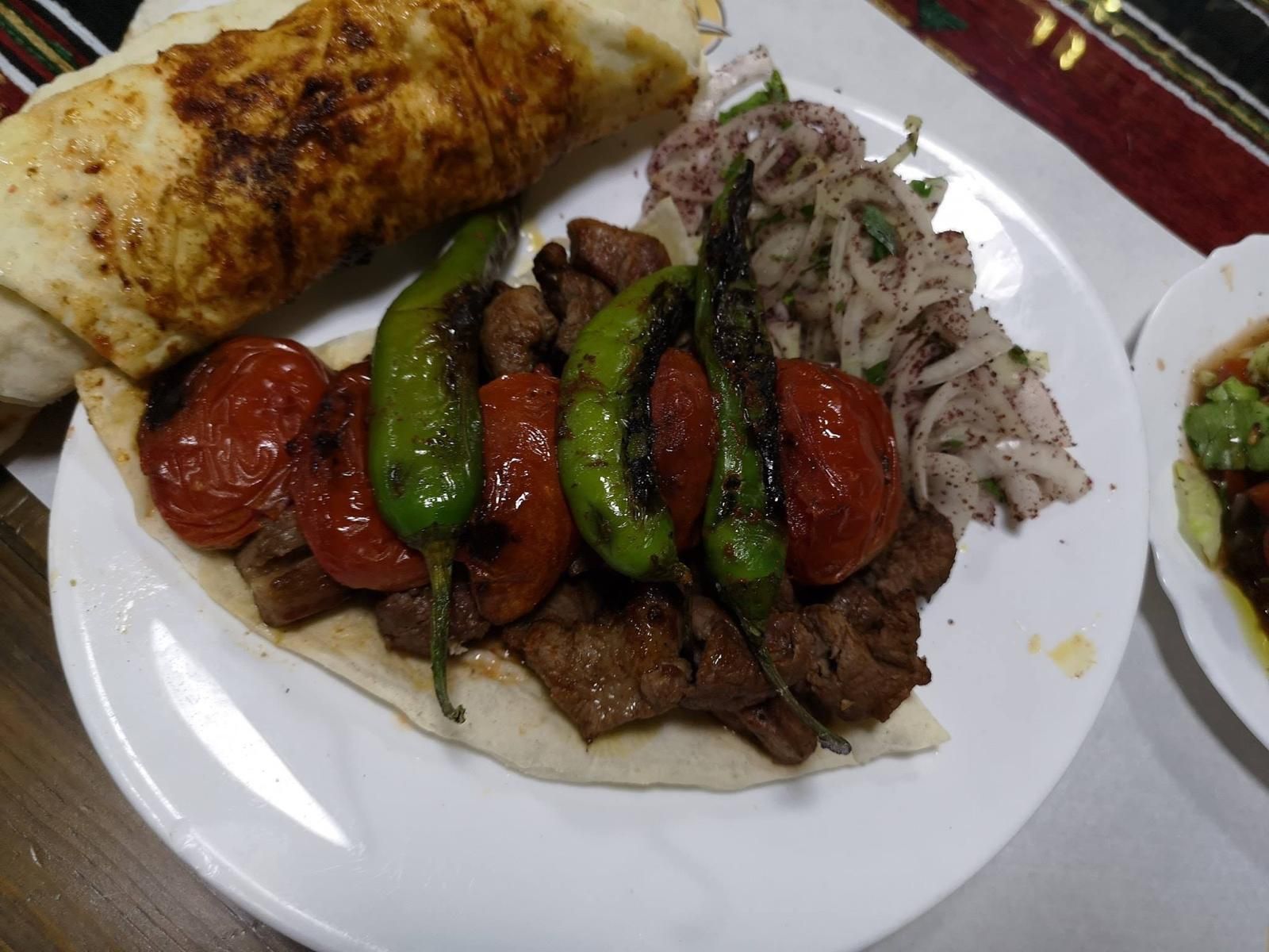 Piatto di carne alla griglia, pomodori e peperoni con insalata di cipolle e pane piatto.