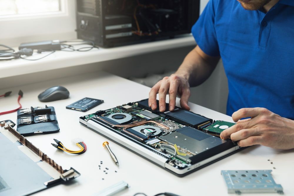 A Man in a Blue Shirt is Working on a Laptop Computer — Leading Edge Computers in Forster, NSW