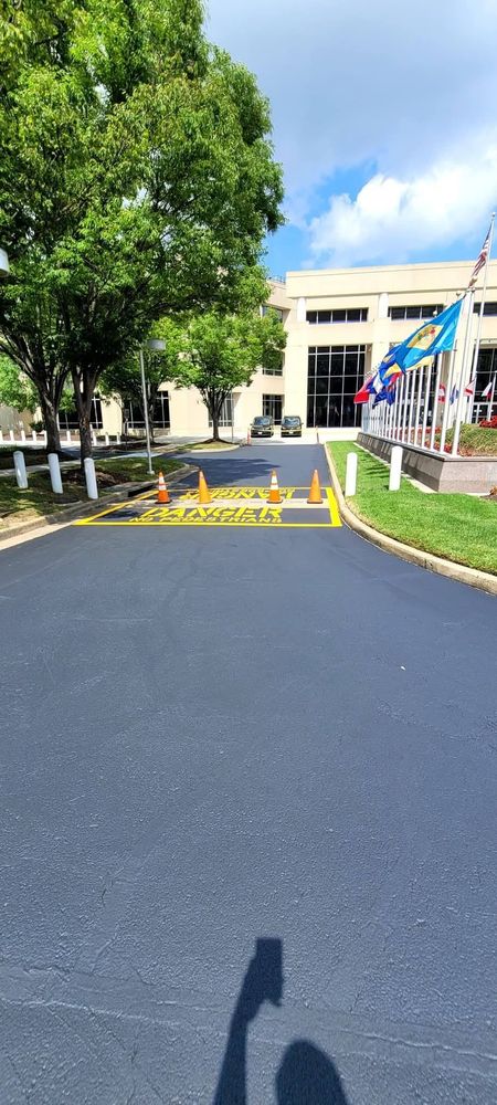 Asphalt driveway leads to a building, with trees and flags. Construction zone with cones in the middle. Sunny day.