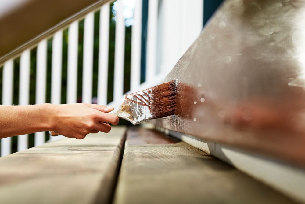 A person's hand painting a wooden deck railing brown.