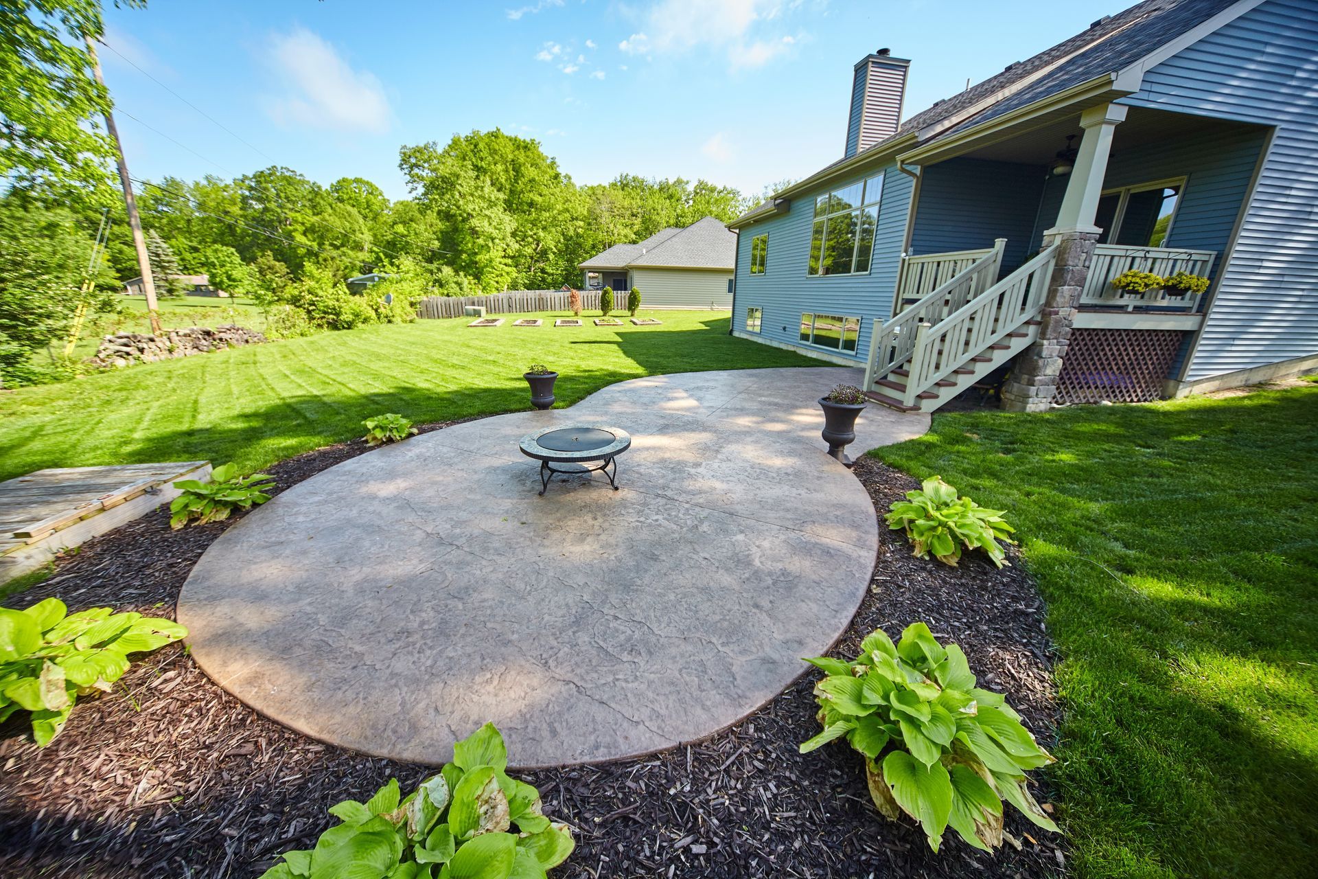 Backyard patio with fire pit, landscaping, and blue house.
