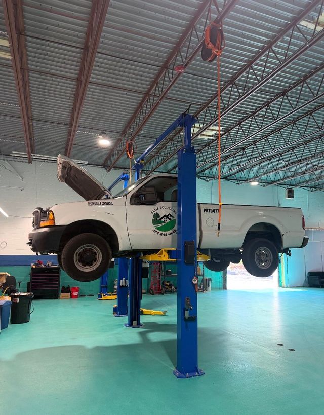 White pickup truck lifted on a blue hydraulic lift in an auto repair garage | JKR Automotive Solutions