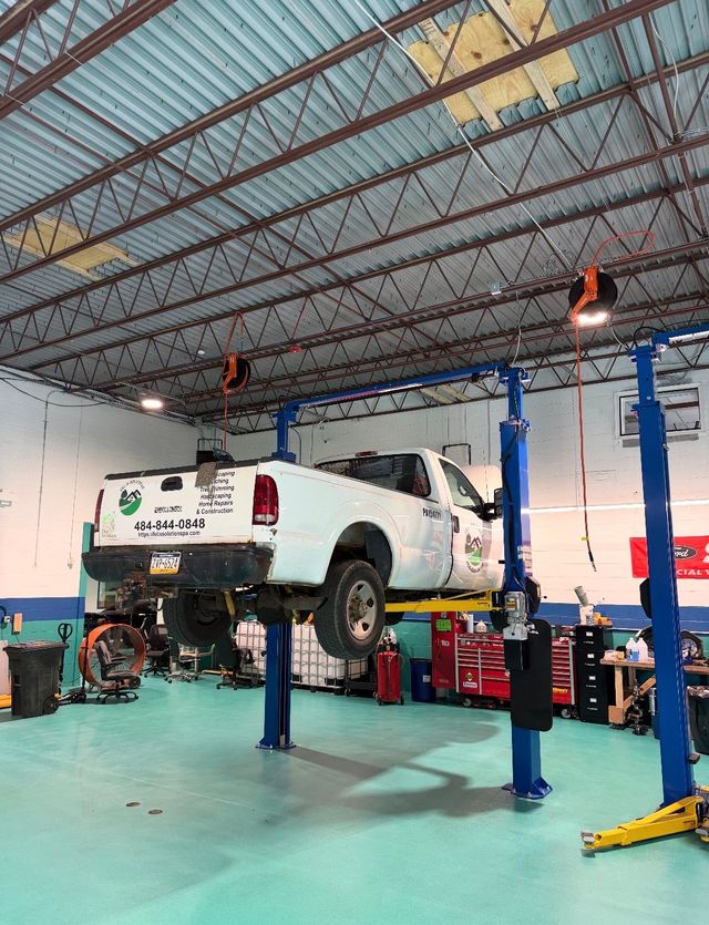 White pickup truck raised on a blue lift inside an auto repair garage with tools and equipment nearby | JKR Automotive Solutions