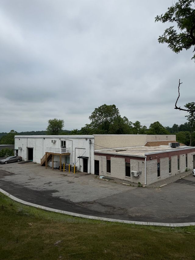 Small white building complex with a gravel lot and overcast sky, surrounded by trees. | JKR Automotive Solutions