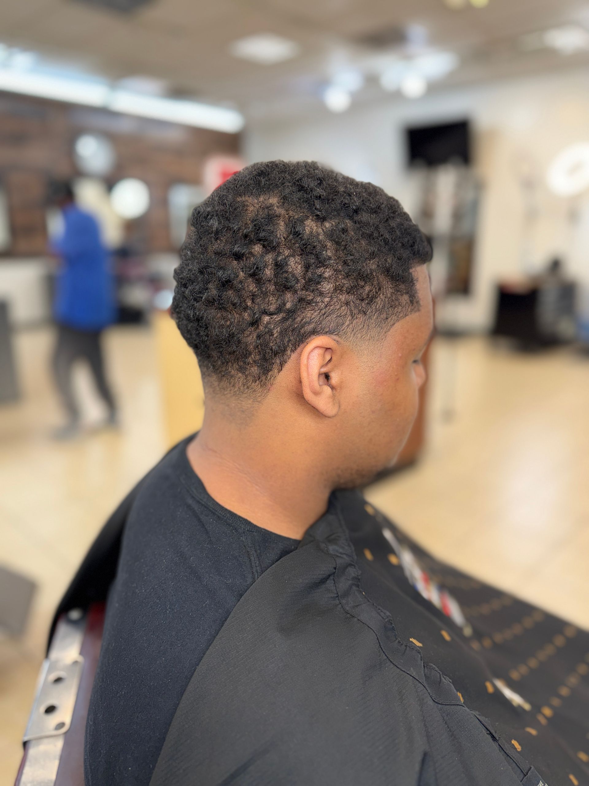 A person with a short, textured haircut with a clean fade around the ears and neck, sitting in a barbershop chair.