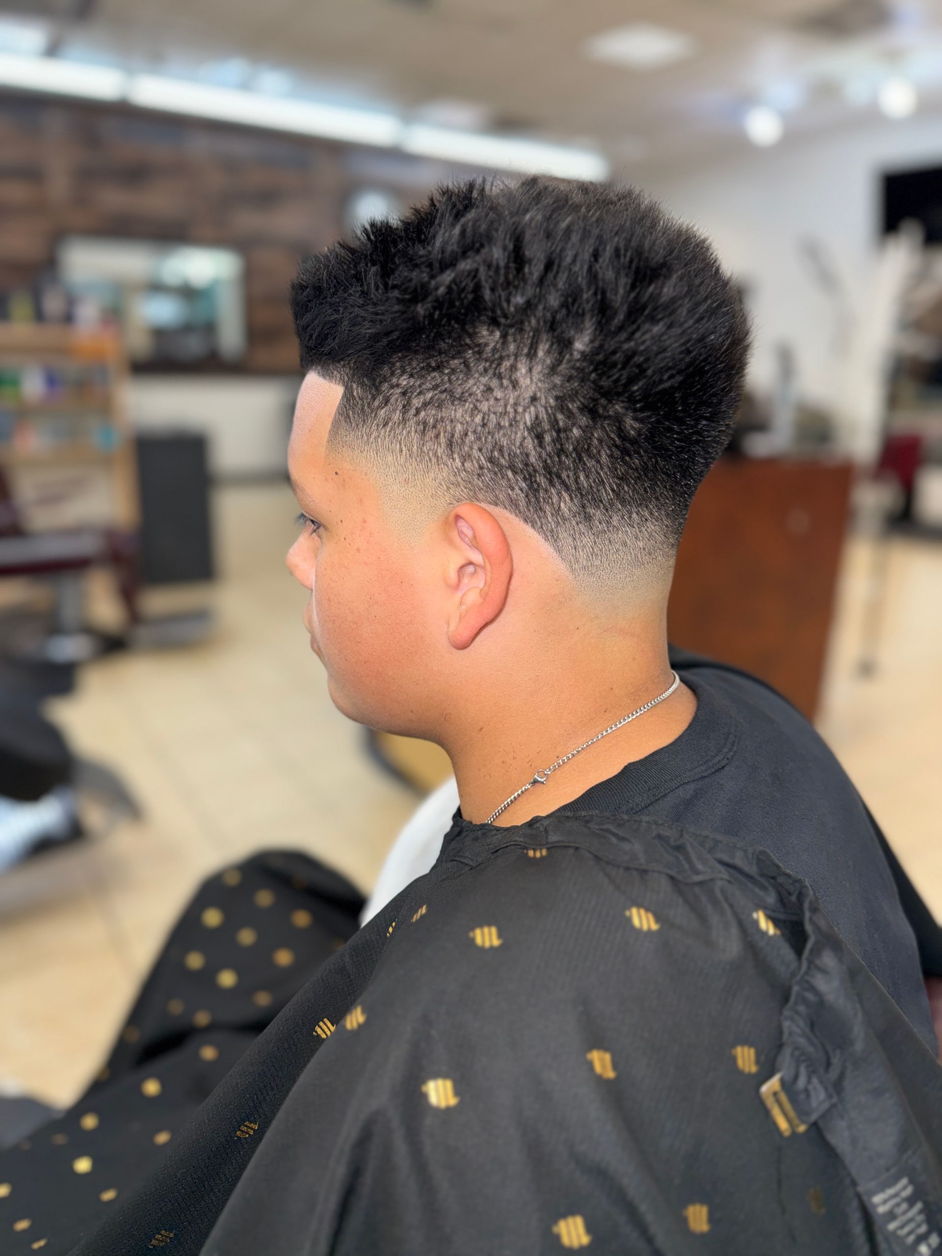 Profile view of a fresh, short taper fade haircut with textured hair on top in a barbershop setting.