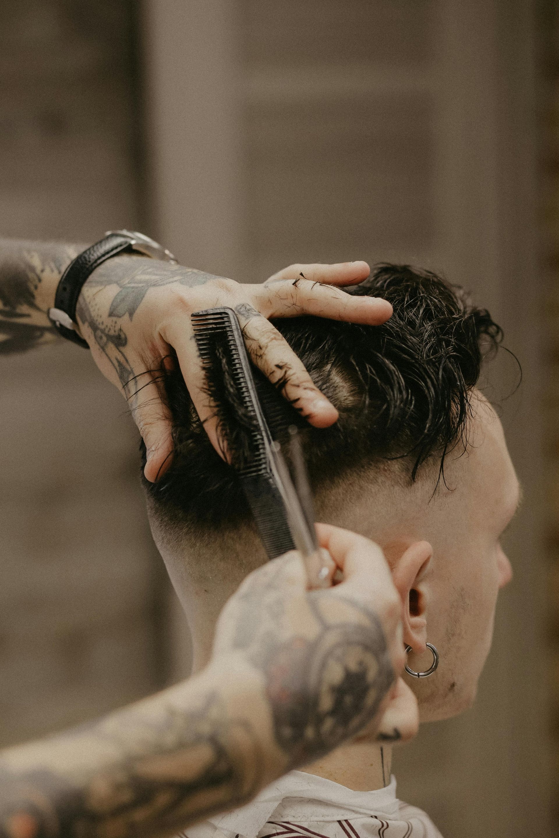 A tattooed barber uses a comb to style the hair of a client during a haircut.