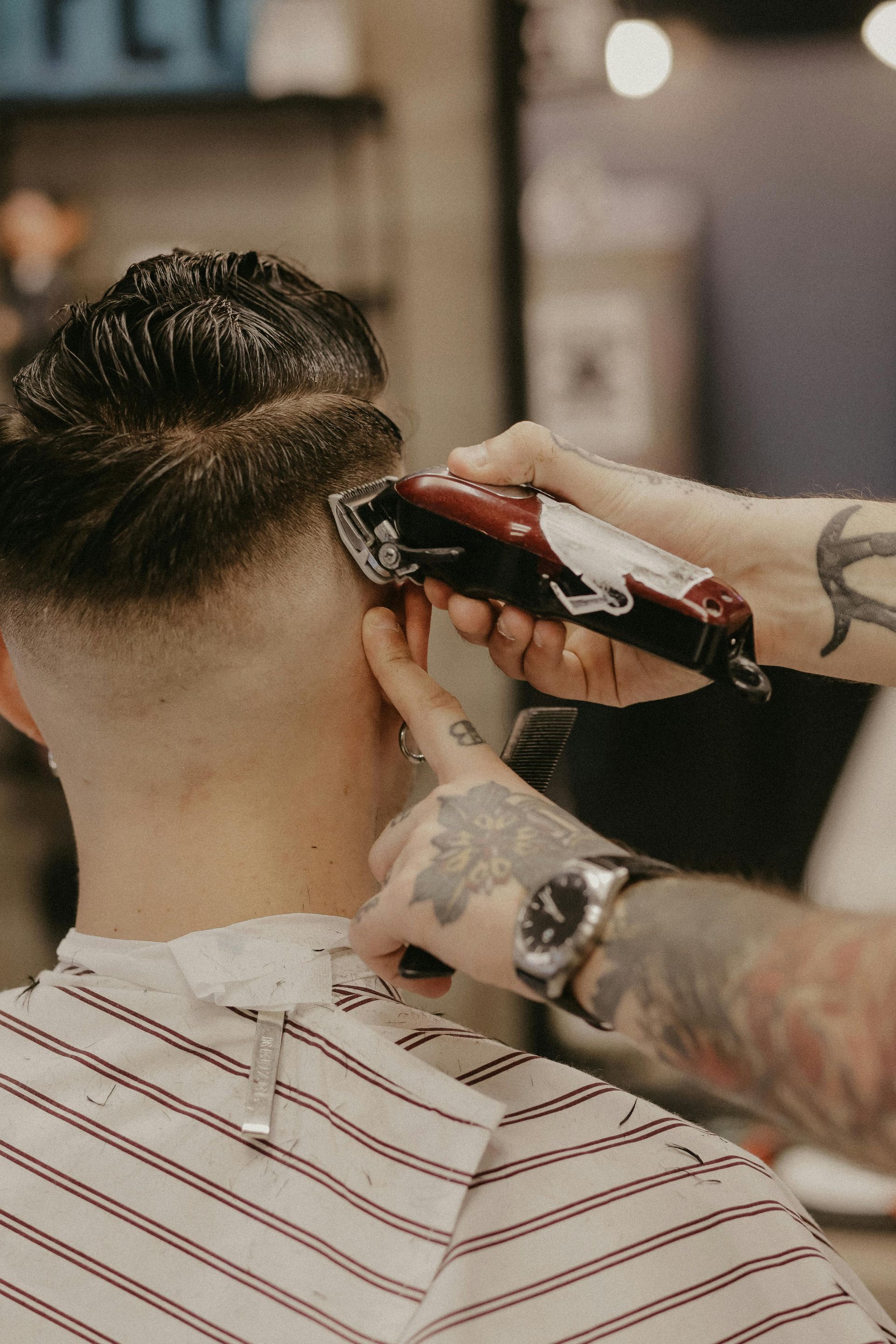 A barber uses clippers to trim the hair on a client's head in a shop.