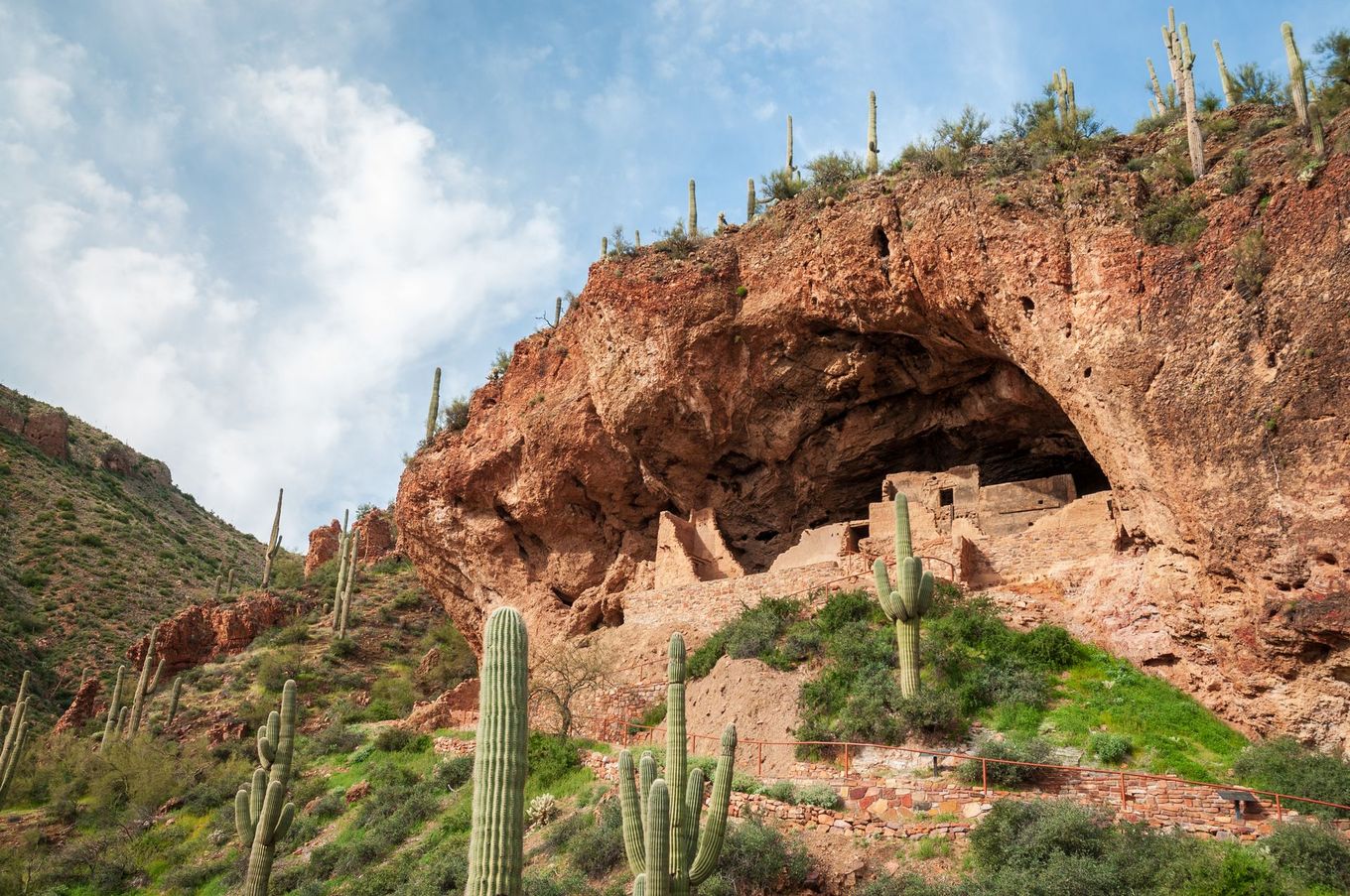Red rock cliff with a large cave-like opening above desert cacti under a blue sky