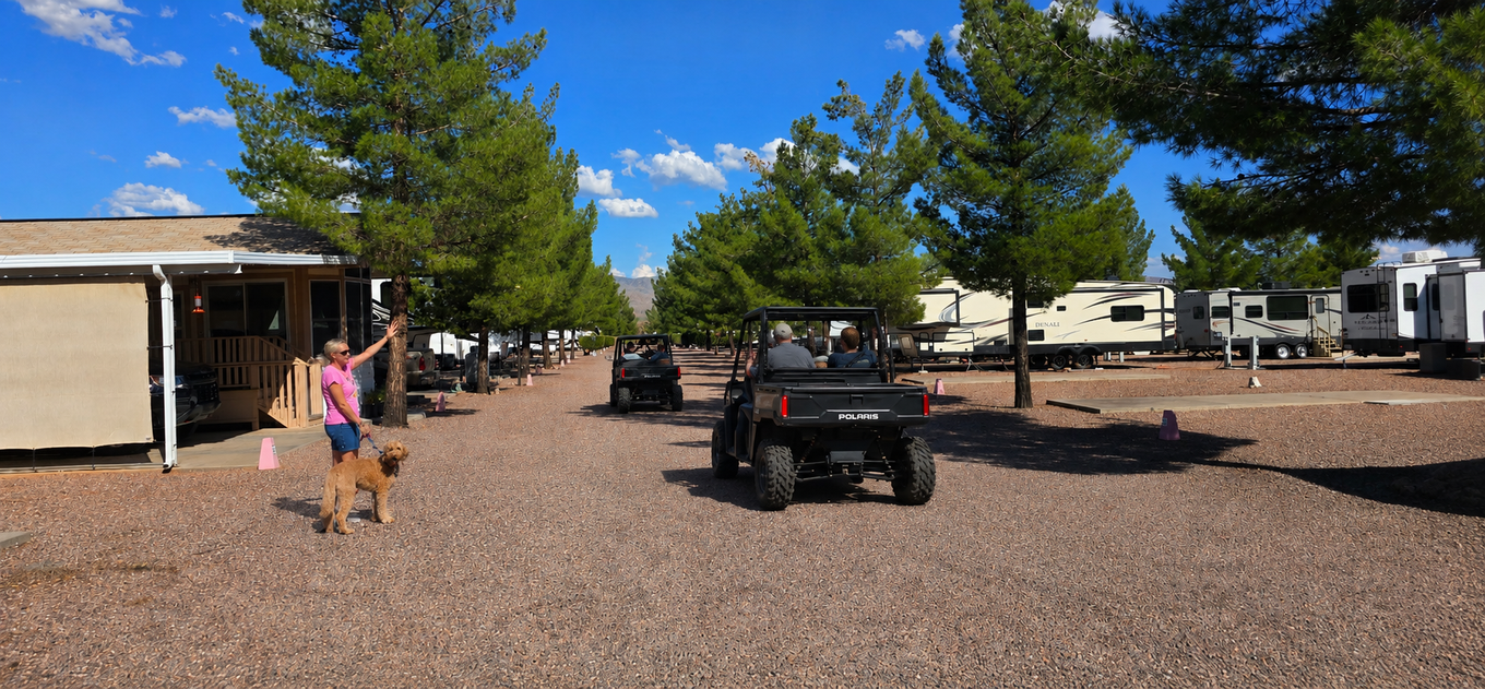 Rural RV park with gravel lot, parked pickup truck, and people walking near a building under a blue sky