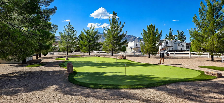 Landscaped park with a curved green lawn, trees, and a blue sky beside residential buildings