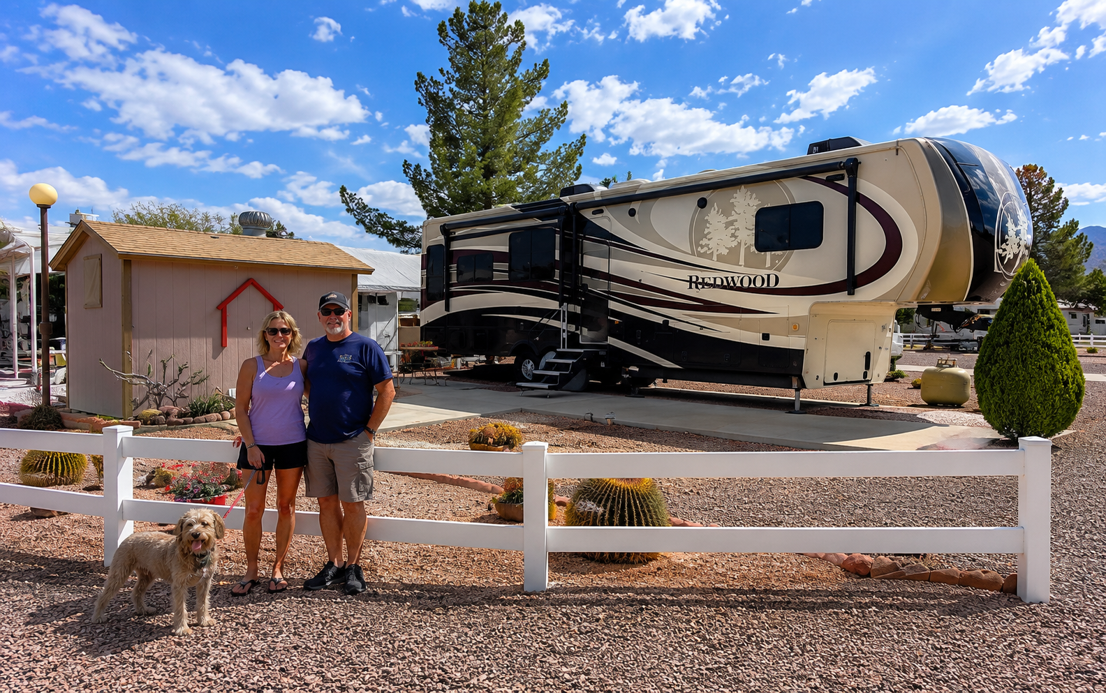 Couple standing by white fence in front of a large RV at a desert campground
