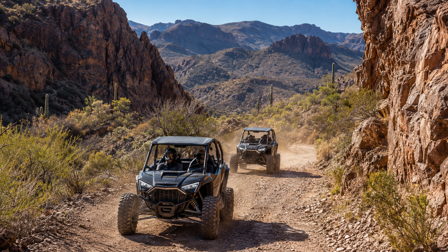 Two off-road vehicles driving through a rocky desert canyon on a dusty trail