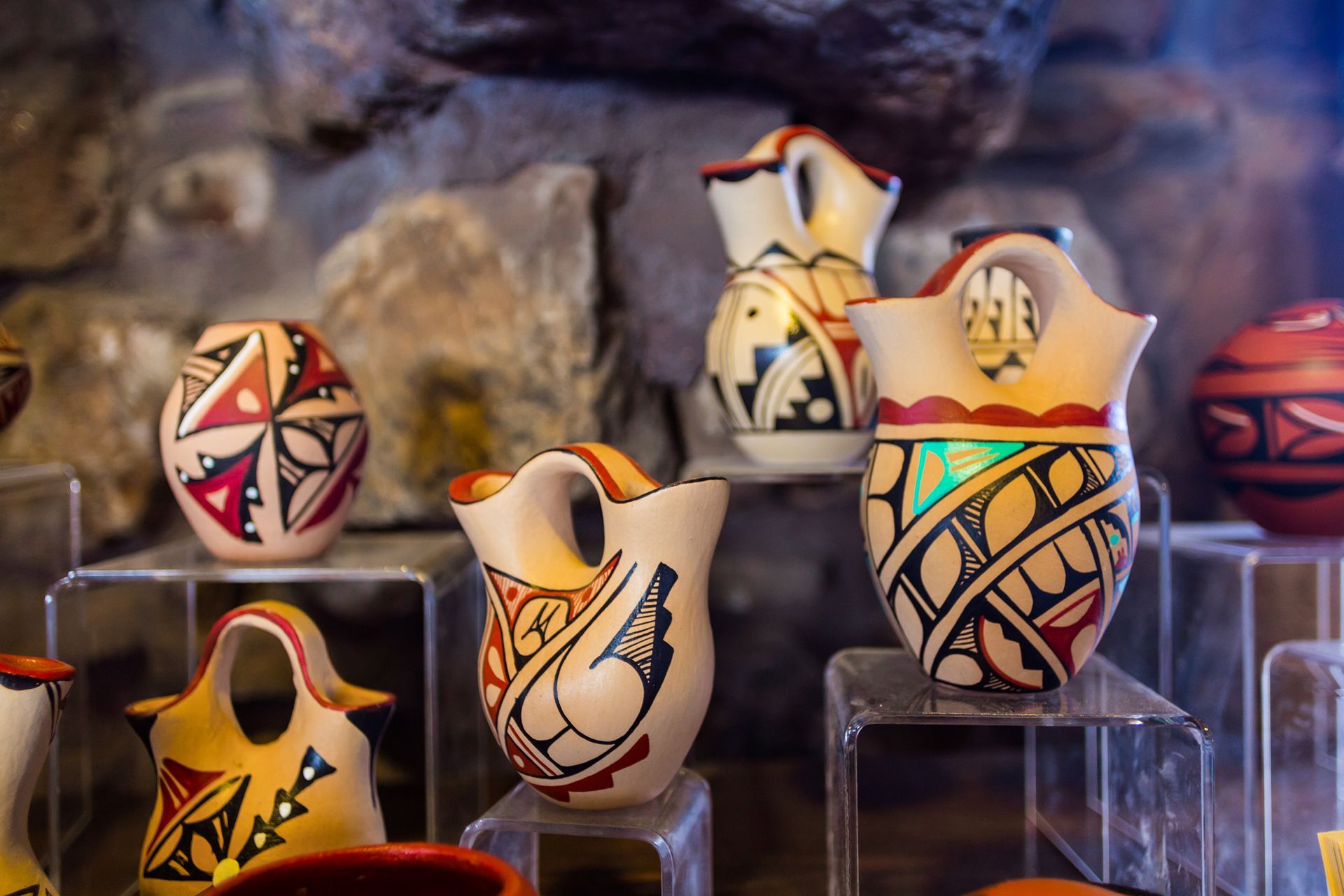 Decorative painted pottery vessels on clear stands, with colorful geometric patterns against a stone backdrop