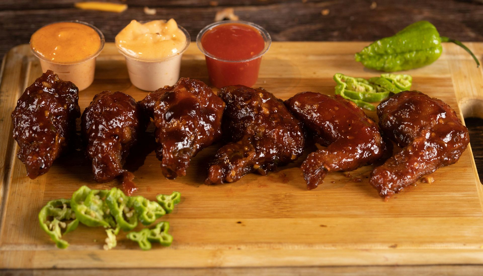 Barbecue chicken wings with three dipping sauces on a wooden board, garnished with lettuce and herbsdefault image