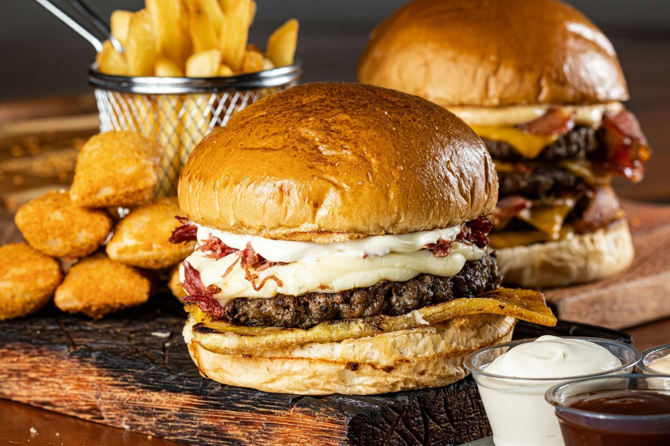 Burgers, fries, onion rings, and dipping sauces on a wooden board