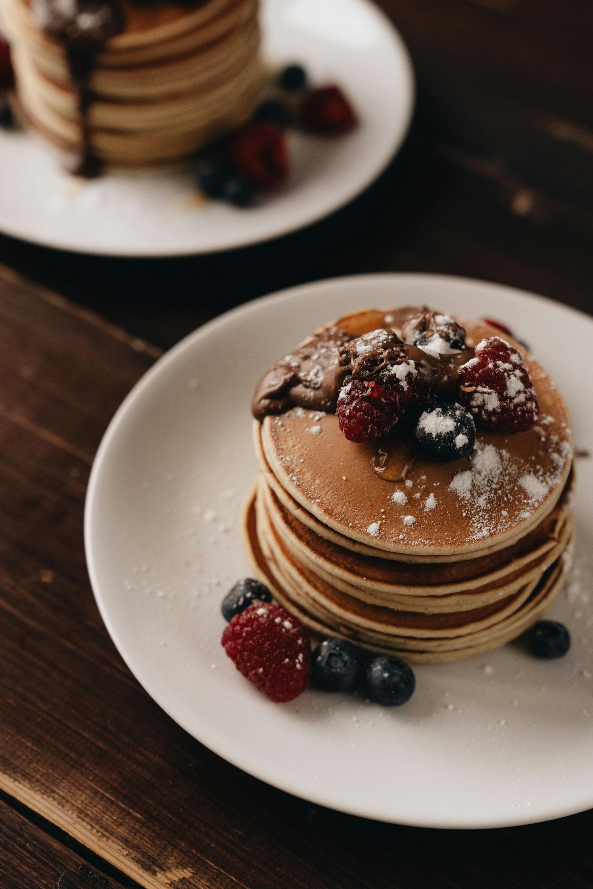 Stack of pancakes topped with berries and powdered sugar on a white plate