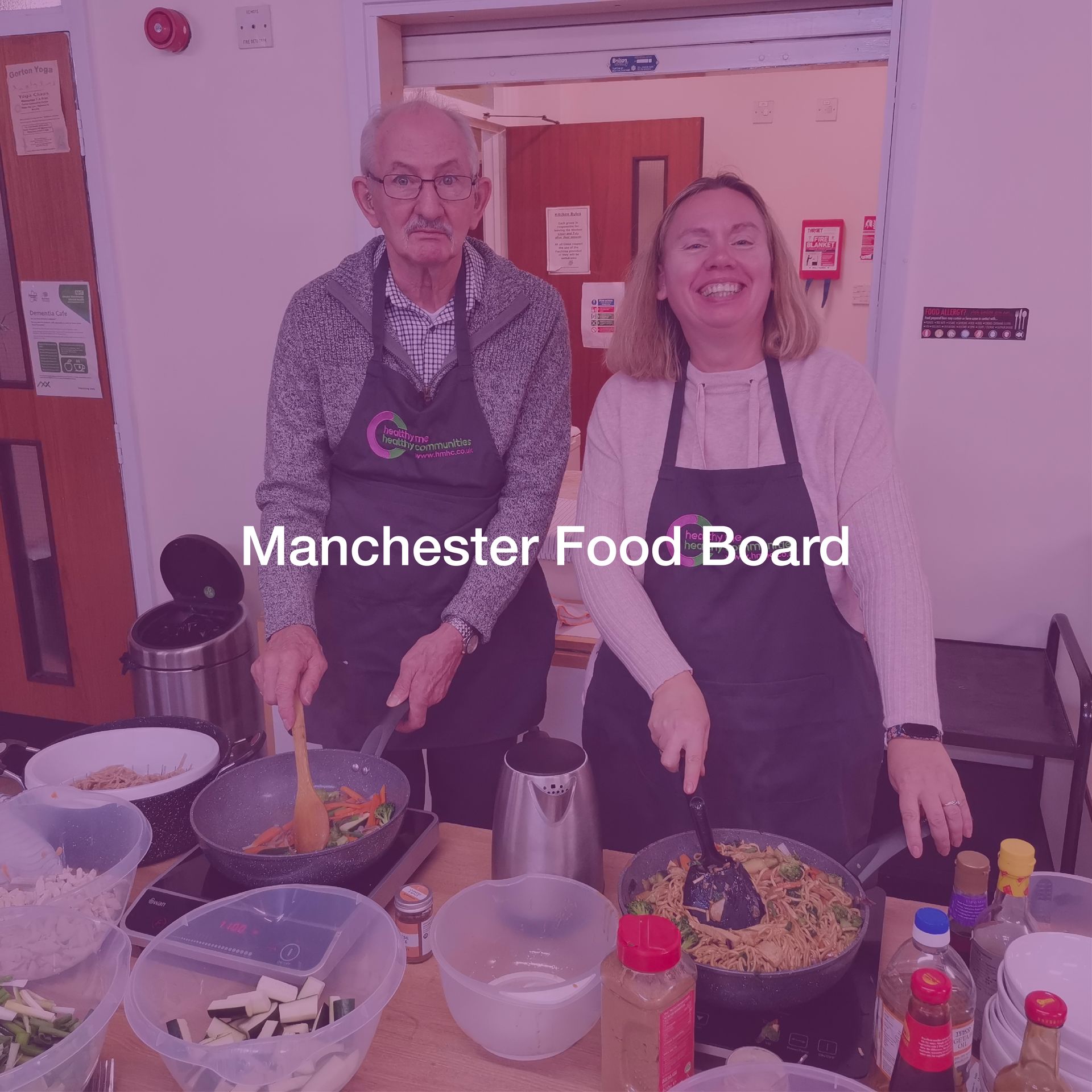 A man and a woman are standing next to each other in front of a manchester food board sign