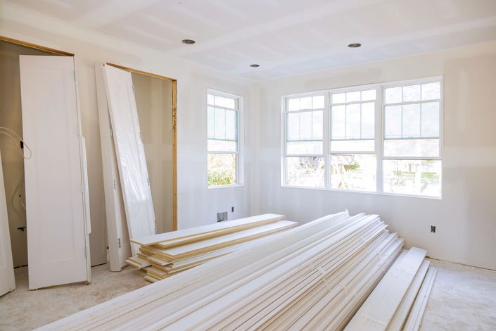 Interno di una stanza in costruzione con pareti in cartongesso bianco, una grande finestra ad arco e telai delle porte non rifiniti.
