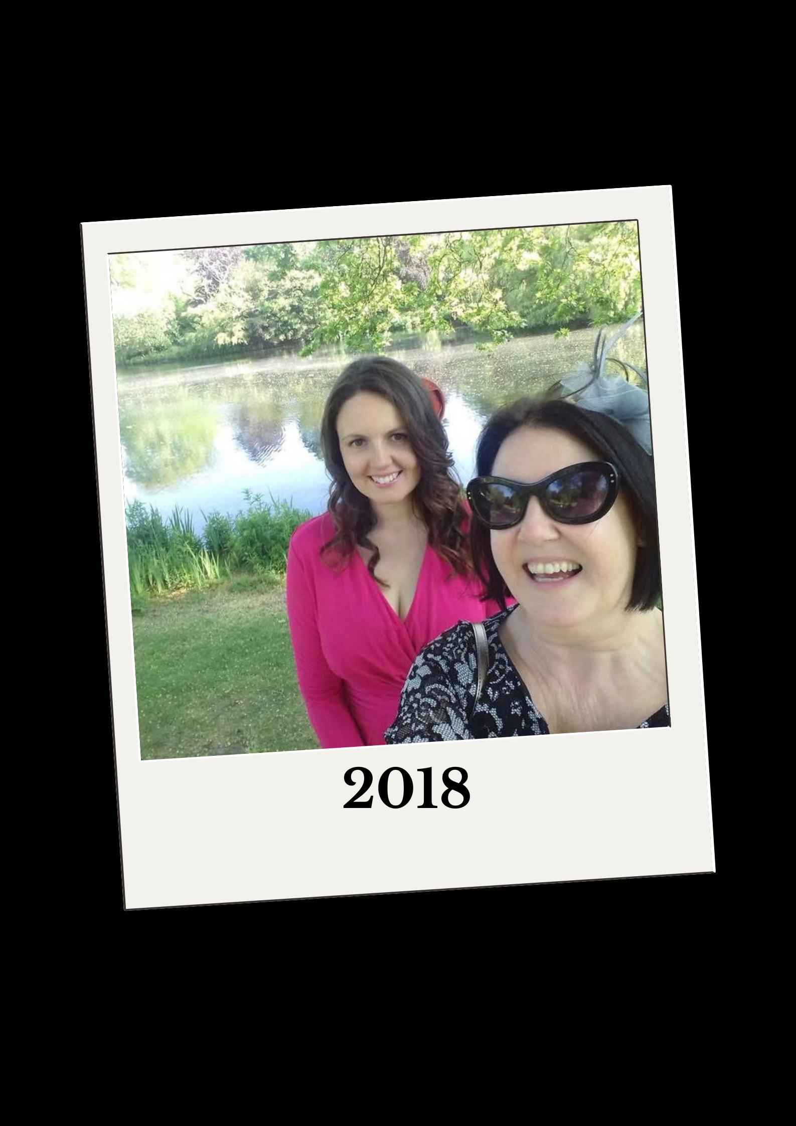 Lisa smiling outside some water with her mum. She is wearing a pink dress.