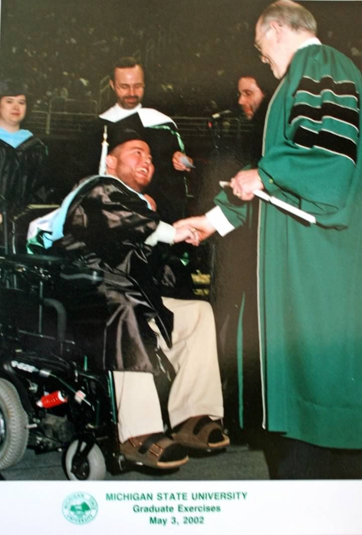 Man in wheelchair shaking hands at Michigan State University graduation, May 3, 2002.